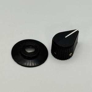 May include: Black guitar amplifier knob with a white indicator line and a matching black washer. The knob has a ridged texture around the sides. The washer has a circular shape with a hole in the center.