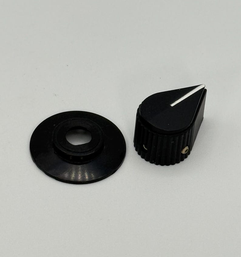 May include: Black guitar amplifier knob with a white indicator line and a matching black washer. The knob has a ridged texture around the sides. The washer has a circular shape with a hole in the center.