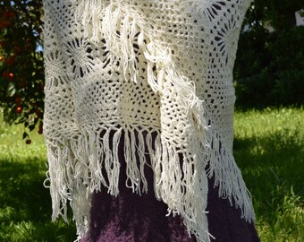 May include: A white crocheted shawl with fringe, draped over a purple dress. The shawl has a delicate floral pattern.