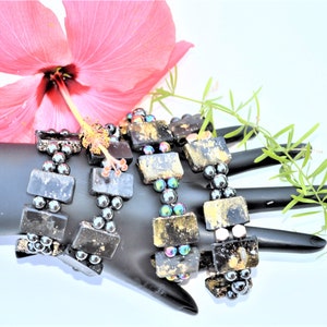 May include: Three black and gold bracelets with black beads. The bracelets are made of square-shaped stones with gold accents and black beads.
