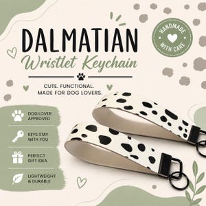 May include: Two wristlet keychains featuring a white background with black spots, resembling a Dalmatian pattern. Each keychain has a black metal clasp and a circular key ring. The text on the image reads DALMATIAN Wristlet Keychain.
