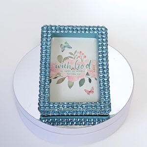 May include: A light blue picture frame with a clear glass insert and a white background with the text "with God all things are possible Matthew 19:26" and a floral design with butterflies.