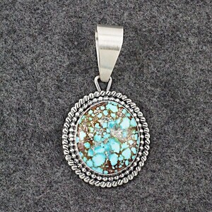 May include: A silver pendant with a turquoise stone set in a beaded border. The stone has a mottled pattern of blue and brown.