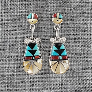 May include: A pair of silver-toned earrings with a colorful inlay design. Each earring features a round top with red, turquoise, and black accents, connected to a teardrop-shaped pendant with similar geometric patterns. The bottom portion is a fan-shaped design.
