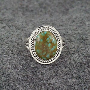 May include: A silver ring with an oval-shaped turquoise stone set in a silver bezel. The stone has a green and brown marbled pattern.
