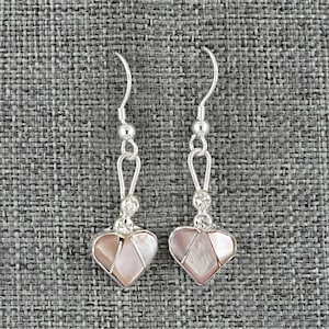 May include: A pair of dangle earrings with a heart-shaped design. The earrings feature a silver-colored hook and chain, with a cluster of small clear stones and a heart pendant made of pink and white iridescent material.