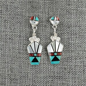 May include: A pair of silver-toned dangle earrings with a geometric design. Each earring features a small, round top with red, turquoise, and silver accents, connected to a larger, stylized pendant with similar colors and patterns.