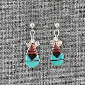 May include: A pair of silver-toned earrings with a teardrop design. Each earring features a turquoise base, a black triangle, a red section, and a cluster of clear stones. The earrings have a post and loop design.