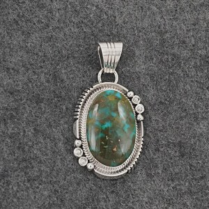 May include: Oval turquoise pendant with a silver setting. The pendant features a large, polished turquoise stone with a mix of blue and brown hues. The silver setting has a decorative border and small, round accents.
