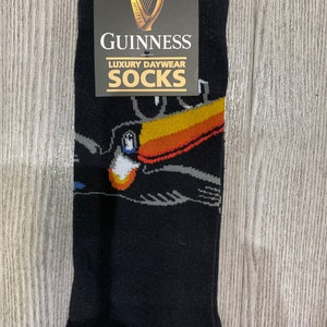 Könnte beinhalten: Schwarze Socken mit einem Tukan-Motiv und einem weißen Etikett mit dem Text "GUINNESS LUXURY DAYWEAR SOCKS".