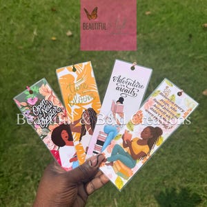 May include: Four colorful bookmarks with inspirational quotes and illustrations. One bookmark reads "Open a New Chapter" with floral accents. Another says "Time to Bloom" with a woman illustration. The third says "Adventure awaits". The last one says "Between every page, she found pieces of herself she didn't know were missing?"