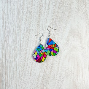 May include: A pair of teardrop-shaped earrings with a colorful stained glass design. The earrings are made of metal and have a silver finish.