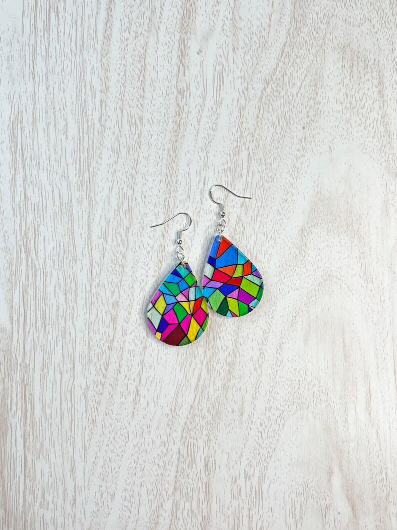 May include: A pair of teardrop-shaped earrings with a colorful stained glass design. The earrings are made of metal and have a silver finish.