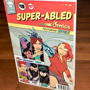 May include: A comic book titled "SUPER-ABLED comics" featuring "REBUILT!" The cover art displays several characters, including a woman with a robotic arm. The comic book has a red and yellow color scheme with the price of $10.