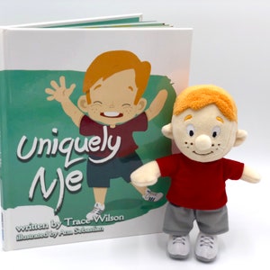 Puede incluir: Un libro infantil titulado "Uniquely Me" con un mu&ntilde;eco de peluche a juego. La portada del libro presenta una ilustraci&oacute;n de un ni&ntilde;o pelirrojo. El mu&ntilde;eco lleva una camiseta roja, pantalones cortos grises y zapatillas blancas.