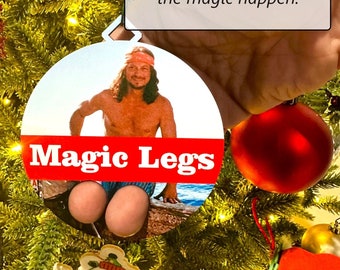 Może przedstawiać: Interaktywna ozdoba choinkowa przedstawiająca mężczyznę z długimi włosami i czerwoną bandaną, z napisem "Magic Legs" w czerwonych literach. Ozdoba jest zaprojektowana do używania z palcami, aby stworzyć iluzję nóg.