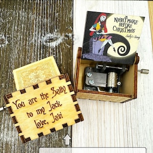 May include: A wooden music box with a hinged lid featuring a printed image of Sally from the Nightmare Before Christmas movie. The lid is open and the music box mechanism is visible. The box has a personalized engraved message that reads "You are the Sally to my Jack. Love, Javi".