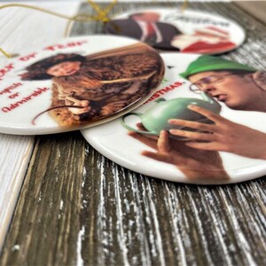 Pode incluir: Tr&ecirc;s ornamentos redondos de cer&acirc;mica com imagens e texto. O primeiro ornamento apresenta uma mulher com um casaco marrom com o texto "Cheer Up, Impish or Admirable". O segundo ornamento apresenta um homem com um chap&eacute;u verde e &oacute;culos segurando um bule verde com o texto "Merry Christmas". O terceiro ornamento apresenta um homem com terno e gravata com o texto "Merry Christmas".