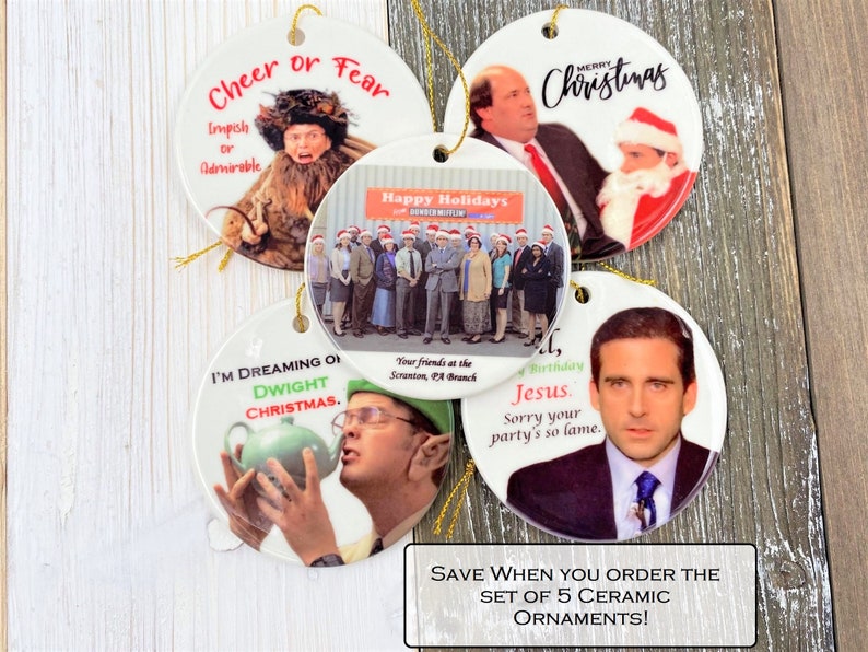 Pode incluir: Conjunto de cinco enfeites de Natal de cer&acirc;mica com personagens e cenas do programa de televis&atilde;o The Office. Os enfeites s&atilde;o redondos e brancos com imagens e texto coloridos. O texto nos enfeites inclui "Cheer or Fear", "Happy Holidays", "I'm Dreaming of Dwight Christmas", "Merry Christmas" e "Birthday, Jesus. Sorry your party's so lame."