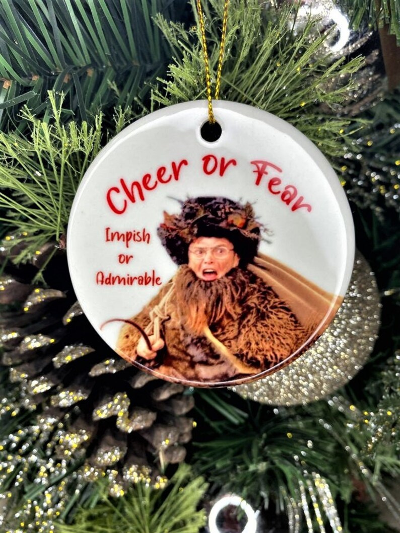 Pode incluir: Enfeite de Natal de cer&acirc;mica branca com uma imagem de uma mulher com uma express&atilde;o de surpresa. O enfeite tem o texto "Cheer or Fear" e "Impish or Admirable" impresso nele.