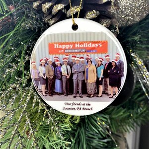 Pode incluir: Enfeite de Natal de cer&acirc;mica branca com uma foto do elenco do programa de televis&atilde;o "The Office" com o texto "Happy Holidays from Dunder Mifflin" e "Your friends at the Scranton, PA Branch".