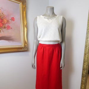 May include: A red midi skirt with a white sleeveless top featuring a lace trim. The top has a delicate pattern.