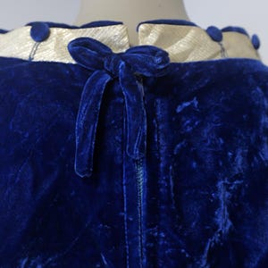 Op de afbeelding: Een blauwe fluwelen jurk met een witte satijnen kraag en een fluwelen strik op de rug. De jurk heeft een rits.