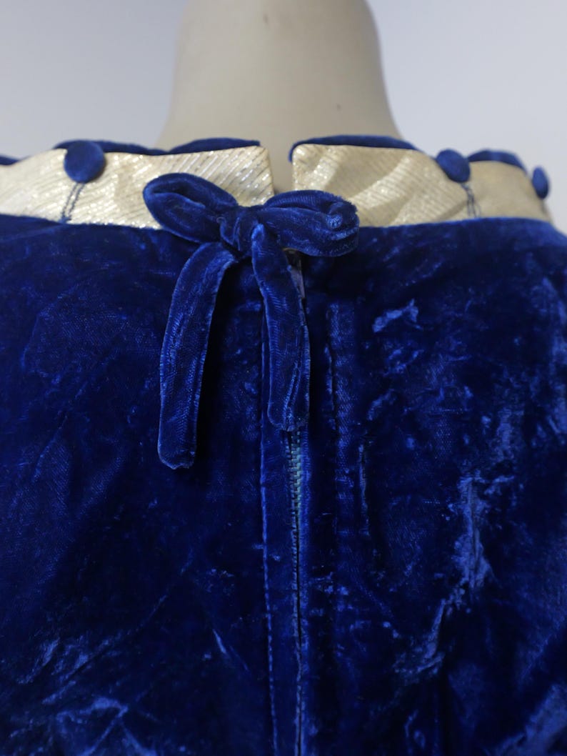 Op de afbeelding: Een blauwe fluwelen jurk met een witte satijnen kraag en een fluwelen strik op de rug. De jurk heeft een rits.