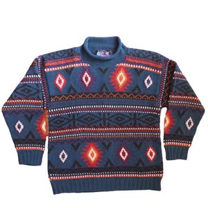 May include: A blue turtleneck jumper with a geometric pattern in red, orange, white, and black. The jumper features diamond and zigzag designs, with ribbed cuffs and hem. A cosy, patterned knitwear garment.