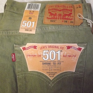Op de afbeelding: Een groene Levi's 501 jeans met een bruin leren label waarop "Levi Strauss & Co." en "501" staat met een taillemaat van 96,5 cm en een lengte van 76,2 cm. De jeans heeft een label met de tekst "Levi's Original Fit 501" en "Straight Leg Button-Fly" met de tekst "America's Original Jeans Since 1973" en "Shrink-to-Fit".