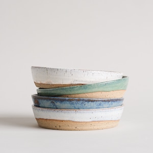 May include: A stack of four ceramic bowls in various shades of blue, green, and white. The bowls are all slightly different sizes and have a rustic, handmade look.
