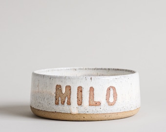 May include: White ceramic pet bowl with a brown rim and the name "MILO" written in brown lettering.