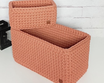 May include: Two rectangular woven storage baskets made of a soft, peach-colored yarn. The baskets are stacked on top of each other.