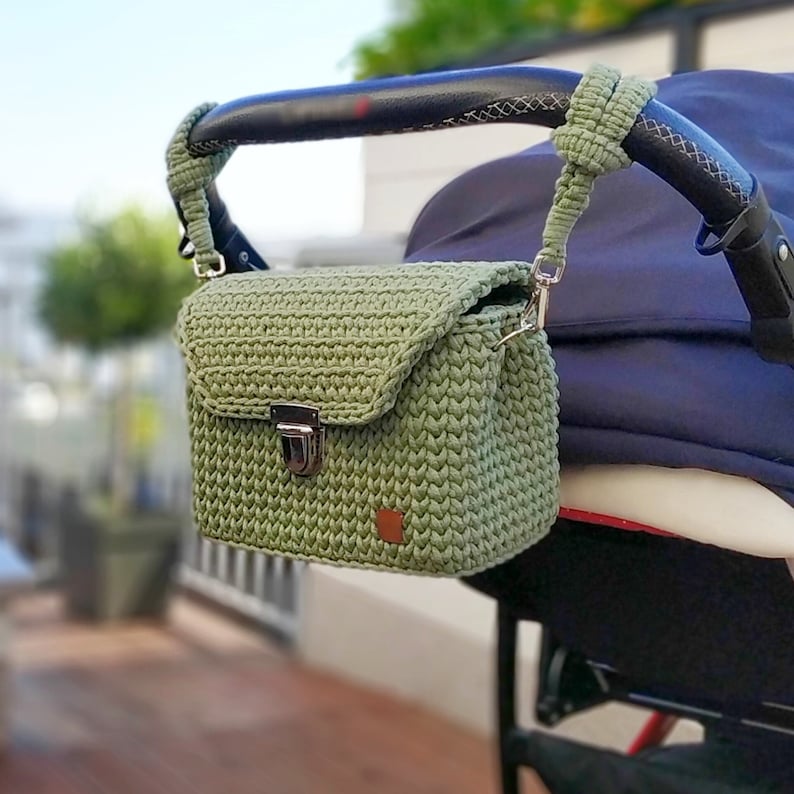 May include: A green crocheted bag with a silver clasp hanging from a stroller handle.