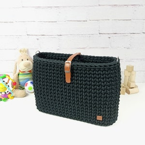 May include: Black crocheted tote bag with a brown leather strap and buckle. The bag has a woven texture and is made of thick yarn.