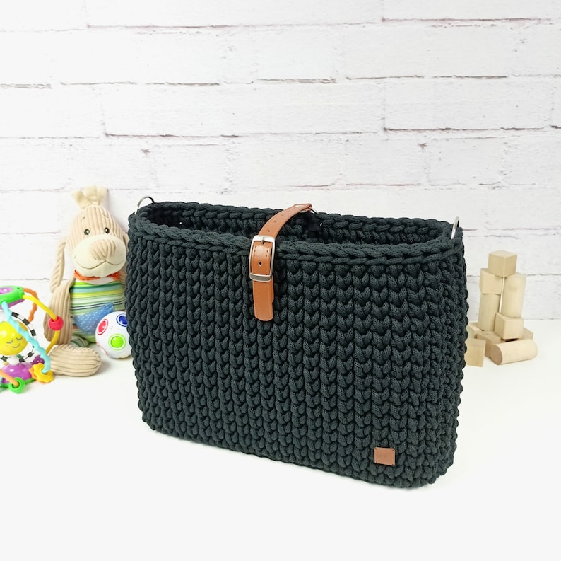 May include: Black crocheted tote bag with a brown leather strap and buckle. The bag has a woven texture and is made of thick yarn.