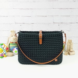 May include: A black crocheted bag with a brown leather strap and buckle closure. The bag has a textured, woven design.