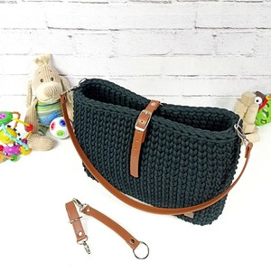 May include: A black crocheted bag with a brown leather strap and buckle. The bag has a long strap that can be adjusted to be worn over the shoulder or as a crossbody bag.
