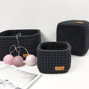 May include: Three black crocheted storage baskets of different sizes. The largest basket is a cube shape. The two smaller baskets are rectangular. The baskets have brown leather labels with the word "Agatka" on them.