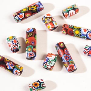 May include: A selection of colourful glass beads with floral and geometric designs. The cylindrical beads display a variety of colours, including red, blue, yellow, and green. These decorative beads are suitable for jewellery making and crafts.