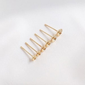 May include: A row of eight gold earring posts with flat, round tops. The posts are arranged in a line, with the tops facing the viewer.