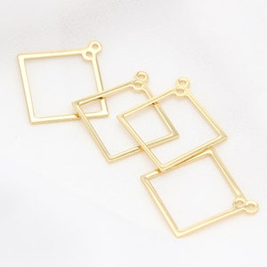 May include: Four gold-colored metal square frames with jump rings. The frames are stacked on top of each other.