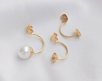 May include: Three gold-toned earring backs with a curved design. One earring back has a white pearl attached.