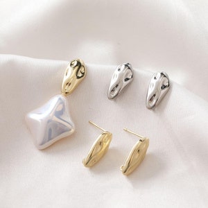 May include: A set of four earrings featuring a unique, abstract design. Two earrings are gold-toned and two are silver-toned. The gold-toned earrings have a pearlescent white stone.