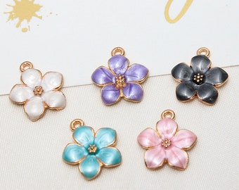 Puede incluir: Seis abalorios de flores de esmalte en diferentes colores, incluyendo morado, negro, blanco, rosa y azul. Cada abalorio presenta un diseño de flor de cinco pétalos con un centro dorado.