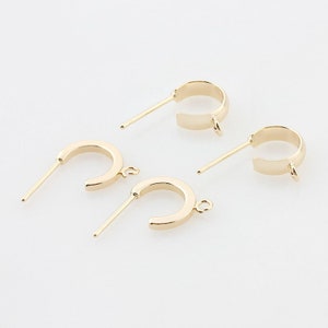 May include: Four gold-colored half-hoop earrings with post backs. The earrings have a simple, minimalist design, featuring a curved, open-ended hoop shape. Each earring has a small loop at the end of the hoop.