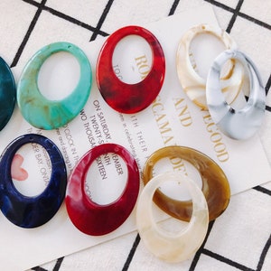 May include: Assortment of oval-shaped resin blanks with a hole at the top. The blanks are in various colors, including red, blue, green, brown, and white. The blanks have a marbled or swirled pattern.