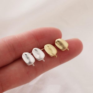 Könnte beinhalten: Drei Paar Ohrring-Verschlüsse in verschiedenen Ausführungen: Silber, Gold und gebürstetes Silber. Die Verschlüsse sind oval geformt und haben eine kleine Schlaufe an der Seite.
