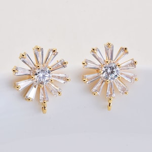 May include: A pair of gold-tone earrings with a clear crystal center and a cluster of smaller crystals around it. The earrings have a dangling design.