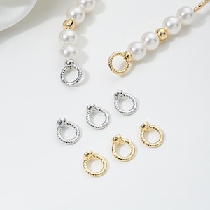 May include: Close-up of jewelry findings, including silver and gold-colored connector rings and pearl strands. The findings are small, circular, and have a textured design. The pearls are white and gold. The image is on a white background.
